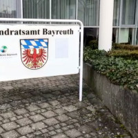 Schild mit Wappen und Aufschrift Landratsamt Bayreuth vor dem Haupteingang des Gebäudes